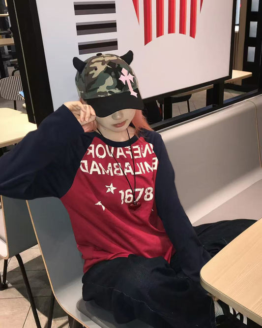 Person wearing a red sweatshirt with text and a camouflage cap sitting on a bench.